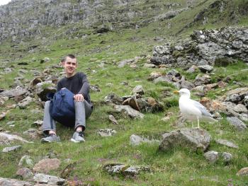 person sitting on rock, while a gull watches