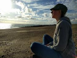 adult sitting on a beach cross-legged, looking out towards the sea