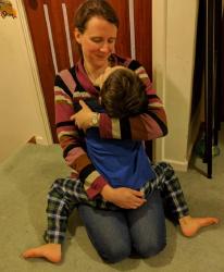 Image of a dark-haired woman with a child on her lap - they are sitting looking at each other, and we can see the woman's face is smiling